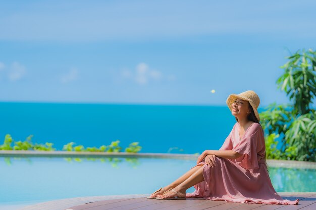 Retrato joven mujer asiática relajarse sonrisa feliz alrededor de la piscina al aire libre en el hotel resort con vista al mar