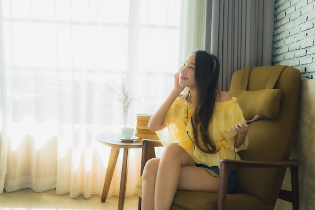 Retrato joven mujer asiática sentarse en la silla escuchar música con teléfono móvil café y libro