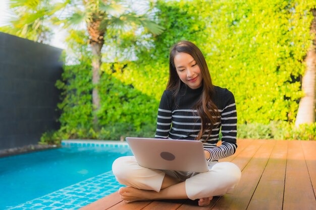 Retrato joven mujer asiática usando la computadora portátil alrededor de la piscina al aire libre