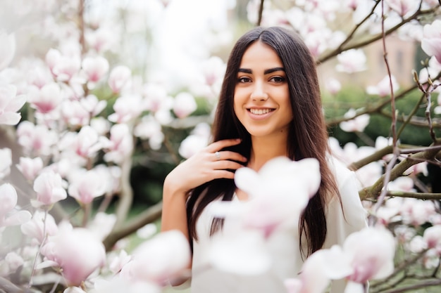 Foto gratuita retrato de joven mujer bonita cerca de la flor del árbol de magnolia en flor. tiempo de primavera