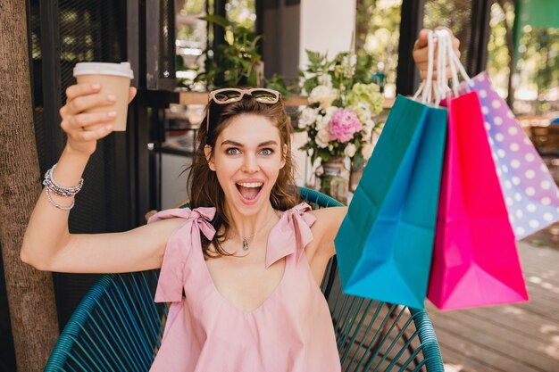 Retrato de joven mujer bonita feliz sonriente con expresión de la cara emocionada sentado en la cafetería con bolsas de compras tomando café