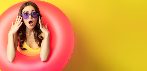 Foto gratuita retrato de una joven mujer bonita con gafas de sol usando un anillo de natación en la playa que parece sorprendida y asombrada