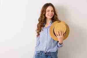 Foto gratuita retrato de joven mujer bonita con sombrero de paja jeans camisa de algodón azul posando en la pared blanca