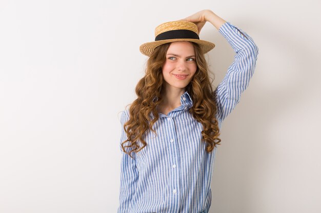 Retrato de joven mujer bonita con sombrero de paja jeans camisa de algodón azul posando en la pared blanca