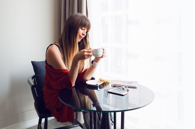 Retrato de joven mujer bonita tomando café, desayunando en casa por la mañana