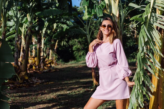 Retrato de joven mujer bronceada caucásica en romántico vestido rosa pendientes redondos pulsera de plata y gafas de sol