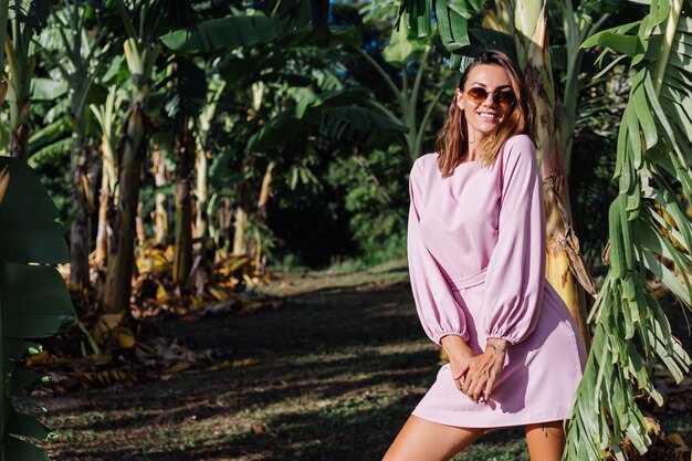 Retrato de joven mujer bronceada caucásica en romántico vestido rosa pendientes redondos pulsera de plata y gafas de sol