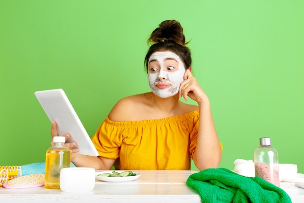 Retrato de joven mujer caucásica en día de belleza, rutina de cuidado de piel y cabello. Modelo femenino haciendo selfie, vlog o videollamada mientras se aplica máscara facial. Cuidado personal, belleza natural y concepto de cosmética.