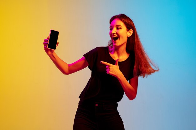 Retrato de joven mujer caucásica sobre fondo de estudio azul-amarillo degradado en luz de neón. Concepto de juventud, emociones humanas, expresión facial, ventas, publicidad. Preciosa modelo morena.