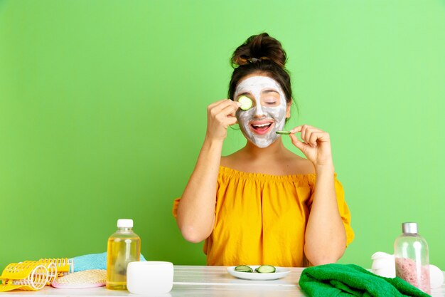 Retrato de joven mujer caucásica en su rutina de belleza día, piel y cuidado del cabello. Modelo femenino con cosmética natural aplicando mascarilla facial para maquillaje. Cuidado corporal y facial, concepto de belleza natural.