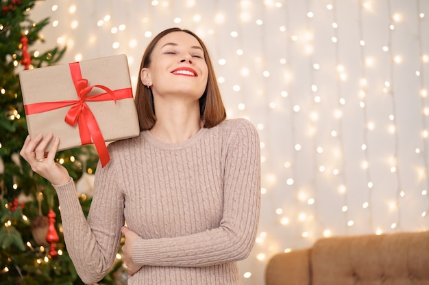 Retrato de joven mujer feliz con labios rojos mirando a la cámara sosteniendo una caja de regalo envuelta