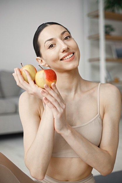 Retrato de una joven mujer fitness en casa sosteniendo manzanas frescas