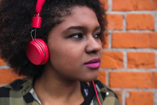 Retrato de joven mujer latina afroamericana escuchando música con auriculares en la calle. Al aire libre.