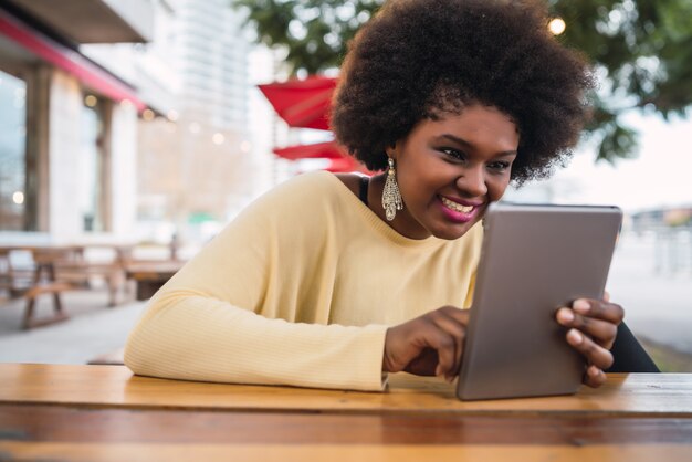 Retrato de joven mujer latina afroamericana usando su tableta digital mientras está sentado en la cafetería. Concepto de tecnología.