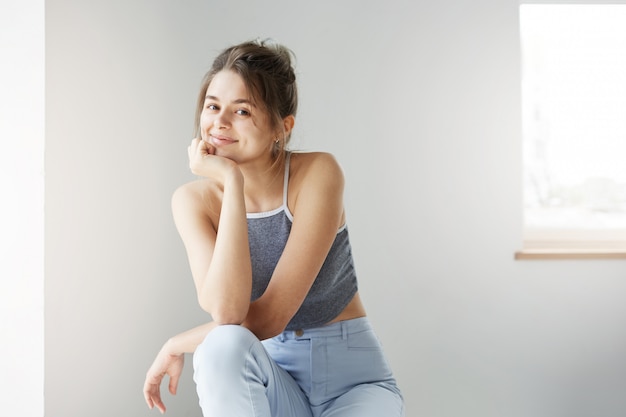 Foto gratuita retrato de joven mujer linda sonriendo sentado en silla sobre pared blanca.