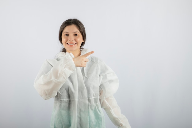 Retrato de joven mujer médico científico en bata de laboratorio defensiva apuntando hacia afuera.