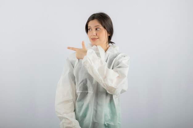 Retrato de joven mujer médico científico en bata de laboratorio defensiva apuntando hacia afuera.