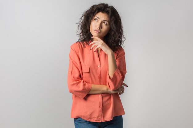 Retrato de joven mujer morena pensativa en camisa naranja, cabello rizado, estilo veraniego, expresión de la cara frustrada, mirando hacia arriba, pensando, problema, idea, raza mixta, aislado