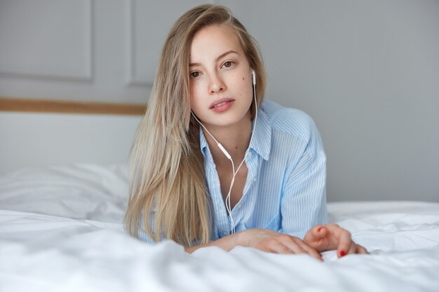 Retrato de joven mujer rubia en la cama con auriculares