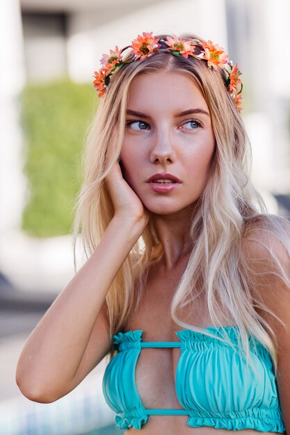 Retrato de joven mujer rubia feliz de pelo largo en bikini azul y corona de flores en la cabeza.