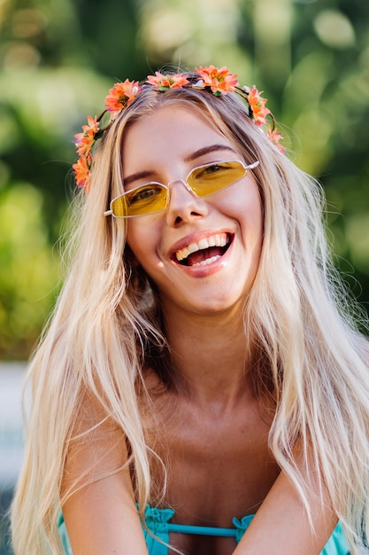 Retrato de joven mujer rubia feliz de pelo largo en bikini azul y corona de flores en la cabeza.