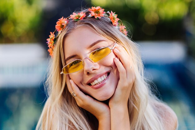 Retrato de joven mujer rubia feliz de pelo largo en bikini azul y corona de flores en la cabeza.