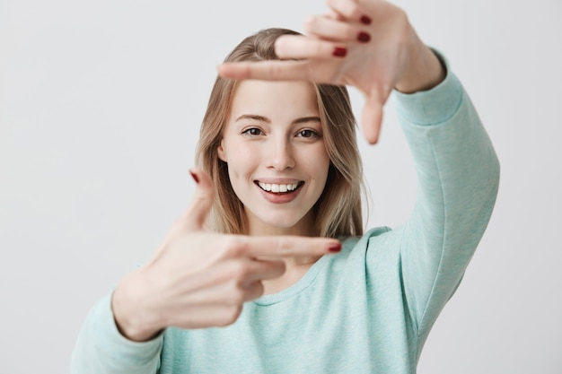 Retrato de joven mujer rubia haciendo gesto de marco con las manos