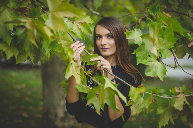 Retrato de una joven mujer rubia posando con hojas de árbol