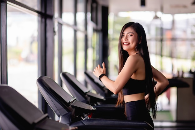 Retrato de joven mujer sana corriendo en caminadora, sonríe durante el entrenamiento en el gimnasio, concepto de estilo de vida saludable, imagen vertical del espacio de copia