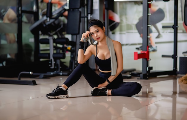 Retrato joven mujer sexy vistiendo ropa deportiva y reloj inteligente sentado en el suelo y limpie el sudor después del entrenamiento en el gimnasio,