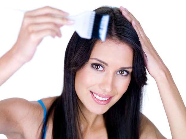 Retrato de joven mujer sonriente coloreando su largo cabello castaño, aislado