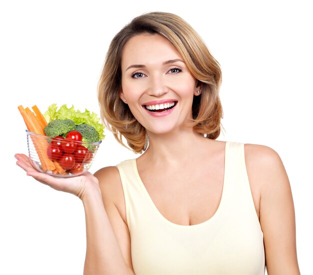 Retrato de una joven mujer sonriente con un plato de verduras aislado en blanco.