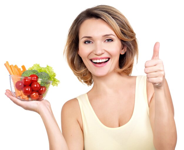 Retrato de una joven mujer sonriente con un plato de verduras aislado en blanco.