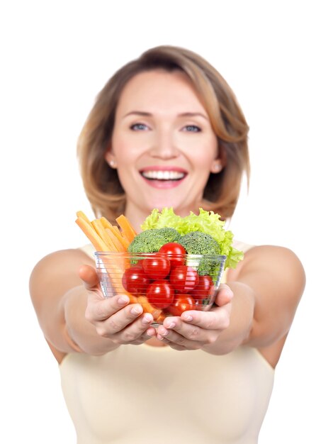 Retrato de una joven mujer sonriente con un plato de verduras aislado en blanco.