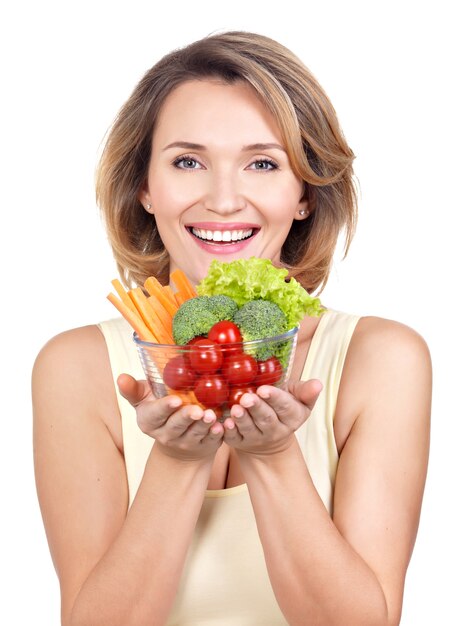 Retrato de una joven mujer sonriente con un plato de verduras - aislado en blanco.