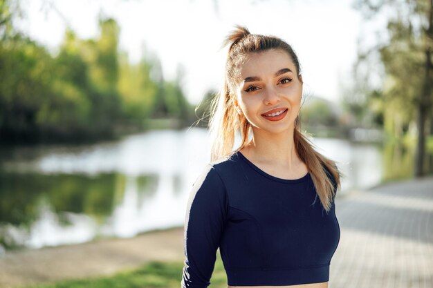 Retrato de una joven mujer sonriente vistiendo ropa deportiva en el parque por la mañana