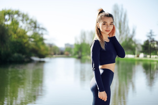 Retrato de una joven mujer sonriente vistiendo ropa deportiva en el parque por la mañana