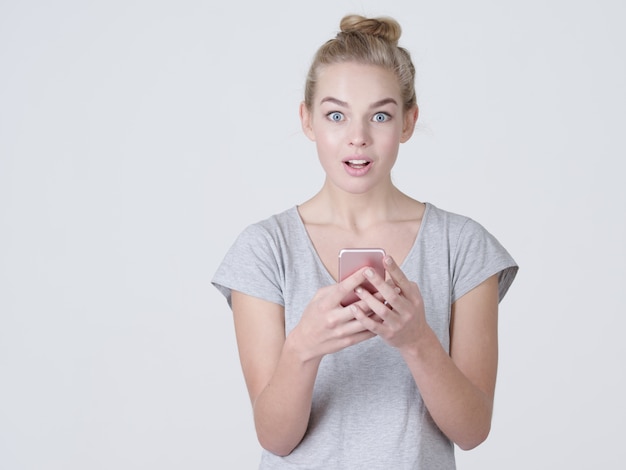 Retrato de joven mujer sorprendida con teléfono móvil en las manos - en el estudio