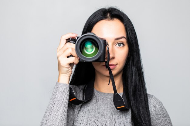 Retrato de una joven mujer tomando fotos en la cámara, aislada en la pared gris