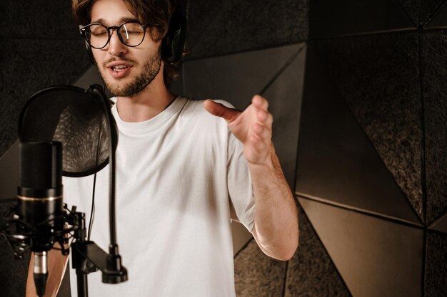 Retrato de un joven músico masculino con auriculares cantando sensualmente grabando una nueva canción en un estudio moderno