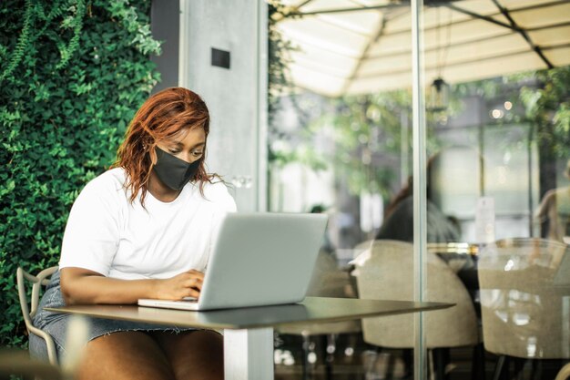 retrato de una joven negra usando una computadora con máscara