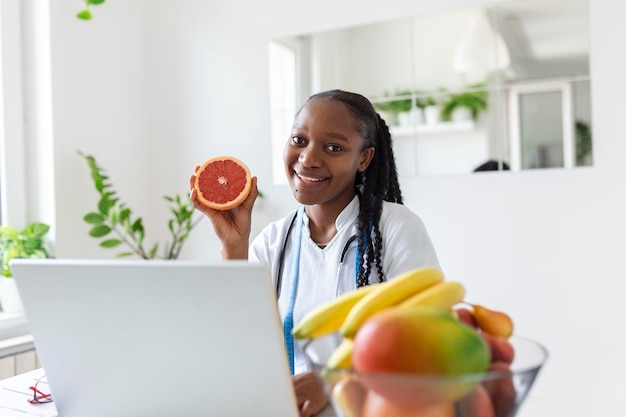 Retrato de una joven nutricionista sonriente en la sala de consulta Escritorio de nutricionista con jugo de fruta saludable y cinta métrica Dietista trabajando en un plan de dieta