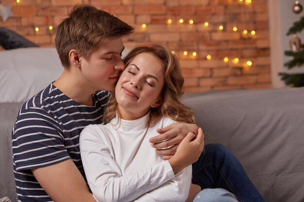 Retrato de una joven pareja amorosa descansando en un sofá gris juntos en casa y abrazándose. se sienten geniales