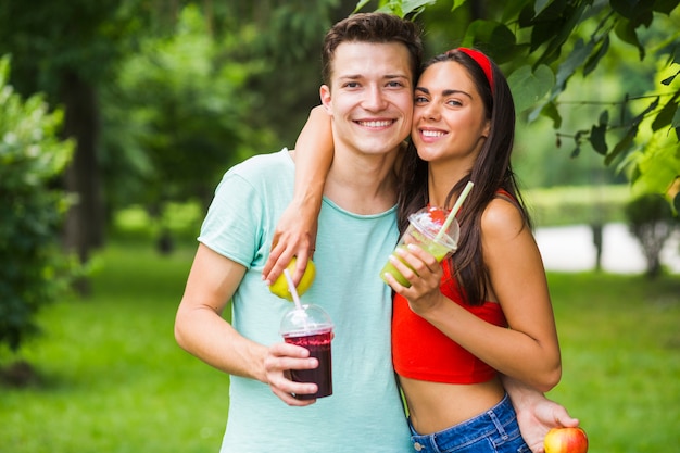 Retrato de la joven pareja con batidos saludables y manzanas en el parque