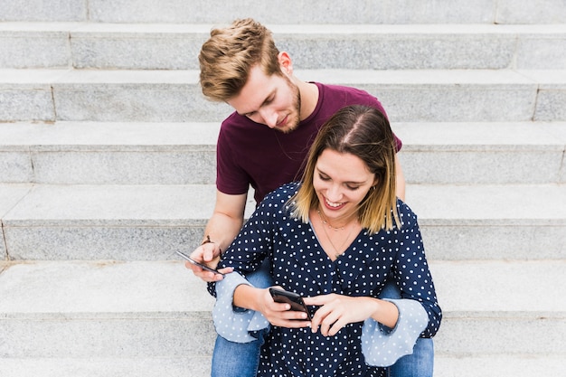 Retrato de una joven pareja feliz sentado en la escalera con teléfono móvil