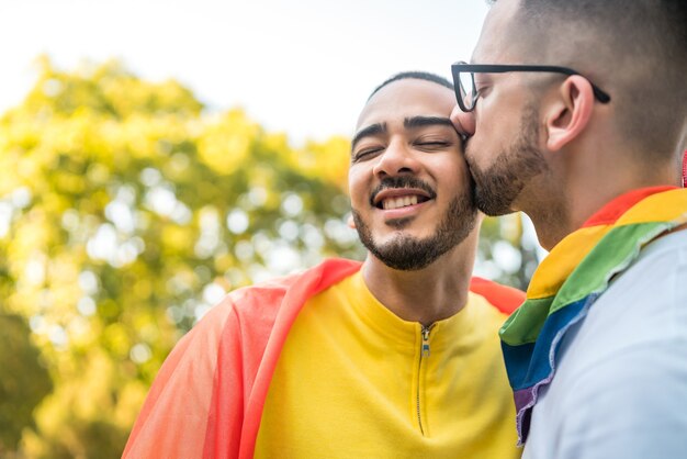 Retrato de joven pareja gay abrazándose y mostrando su amor con la bandera del arco iris en el Stret. Concepto de amor y LGBT.