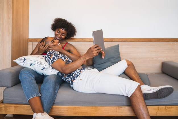 Retrato de joven pareja latina tomando un selfie con tableta digital en casa.