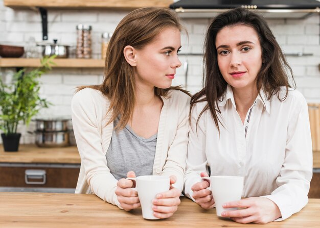 Retrato de joven pareja de lesbianas sosteniendo la taza de café en las manos