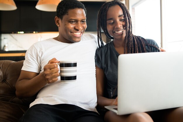 Retrato de joven pareja pasar tiempo juntos y usar la computadora portátil mientras está sentado en el sofá en casa. Nuevo concepto de estilo de vida normal.