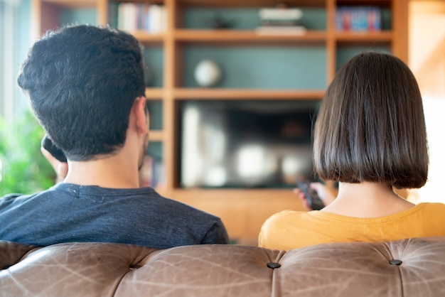 Retrato de joven pareja pasar tiempo juntos y ver series de televisión o películas mientras está sentado en el sofá en casa. Nuevo concepto de estilo de vida normal.